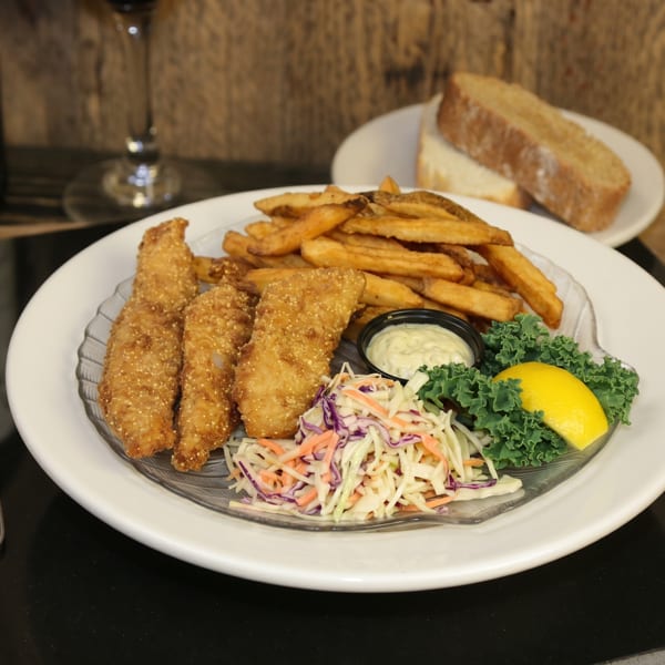 A plate of golden-brown fish and chips with coleslaw, tartar sauce, and a lemon wedge.