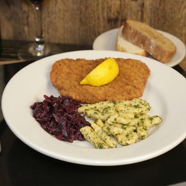 A schnitzel with a lemon wedge, red cabbage, and spaetzle on a white plate.