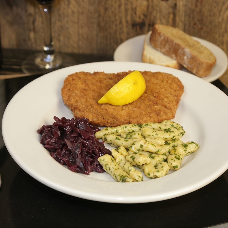 A schnitzel with a lemon wedge, red cabbage, and spaetzle on a white plate.