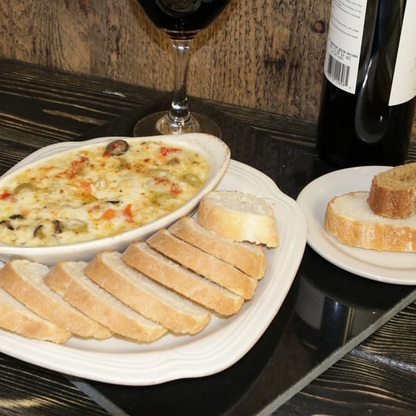 Baked dip with vegetables and cheese, served with sliced baguette and a glass of red wine.