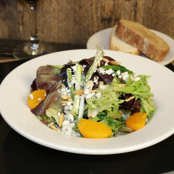 A vibrant salad with mixed greens, mandarin oranges, blue cheese, and almonds, served with bread and wine.